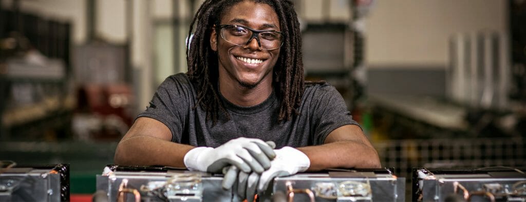 Man smiling in factory with work gloves on.